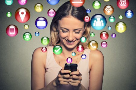 communication technology mobile high tech concept. Closeup happy young woman using texting on smartphone with social media application symbols icons flying out of screen isolated on grey background.
